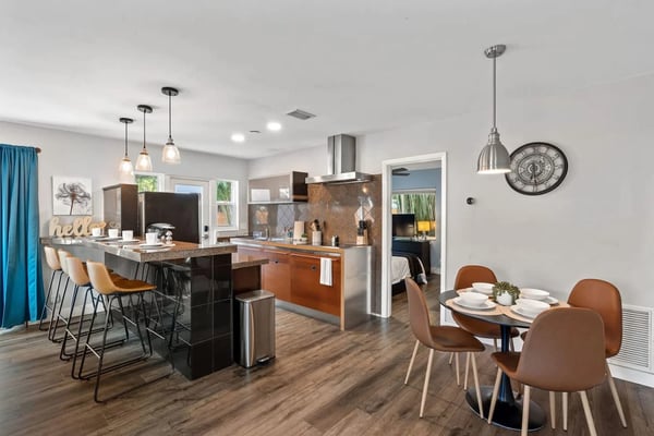 Modern open-plan kitchen and dining area with island seating, pendant lights, and round dining table with brown chairs