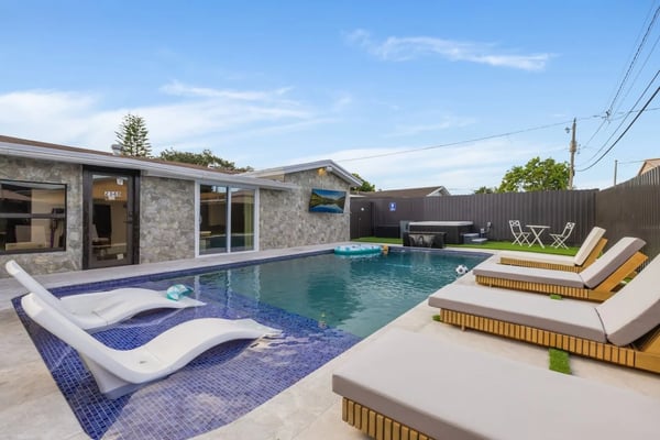 Modern backyard with swimming pool, lounge chairs, and stone house with large windows